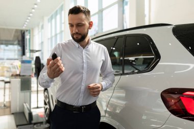 Bir araba galerisinde beyaz gömlekli bir adam elinde beyaz bir cipin yanında tahrik ediliyor.