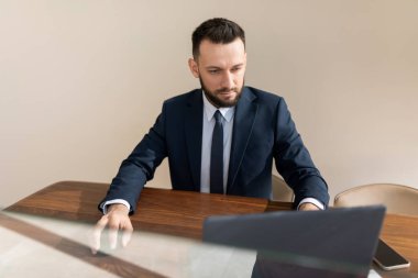 Katı takım elbiseli bir adam ofis duvarlarında dizüstü bilgisayarın arkasında çalışıyor.