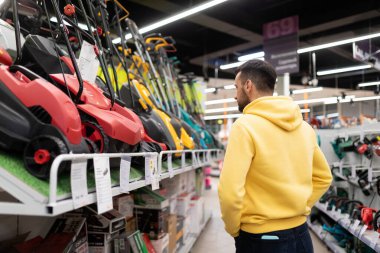Müşteri, bahçıvanlar ve bahçıvanlar için elektrikçi dükkanındaki yeni çim biçme makinesi modellerini inceler.