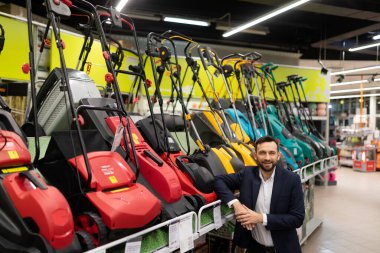 Elektrikli çim biçme makinesi olan bir vitrinin yanındaki bahçe aletleri dükkanının sahibi.