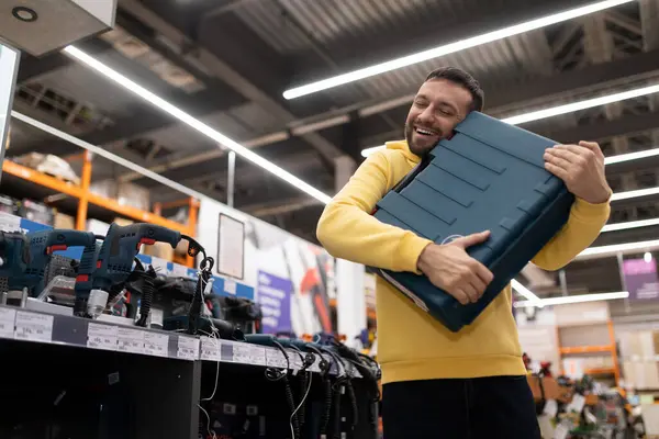 happy buyer of a new electric drill hugging the box in awe in a hardware store