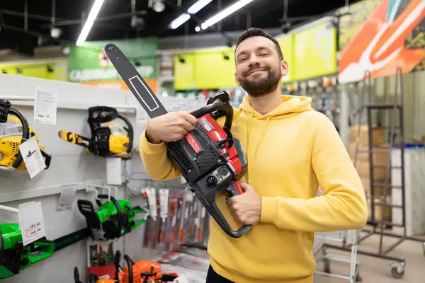 happy buyer in the store with a petrol saw in his hands happy looking at the camera