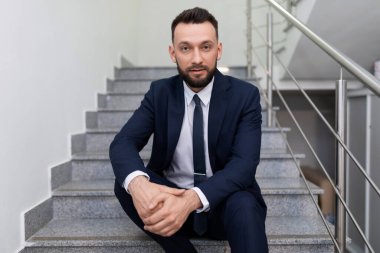 Erkek işadamı merdivenlerde oturuyor ve kameraya giriyor.