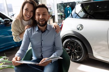 Genç evli bir çift yeni bir araba almadan önce kitapçığı inceliyor. Kişisel ulaşım sigortası kavramı.