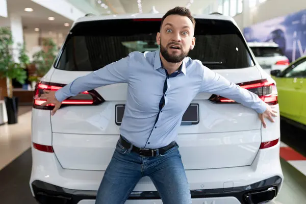 eccentric cheerful man fooling around in a car dealership not wanting to give away his new bought car