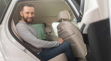 Orta yaşlı bir adam yeni bir arabanın arkasını inceliyor.