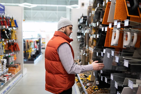 a male builder in a hardware store chooses a spatula for plastering walls