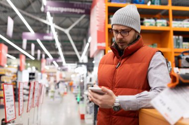 Bir adam ev eşyaları mağazasında telefonundaki çeşitliliği inceliyor..