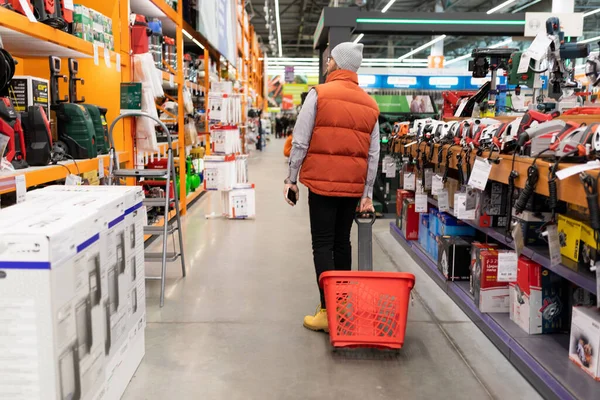 a buyer in a construction hypermarket walks between the rows with a basket on wheels.
