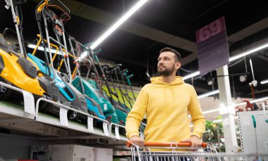 Alışveriş yapan bir adam elinde tramvayla elinde çim biçme makinesiyle beni bahçe malzemeleri dükkanında gezdiriyor..