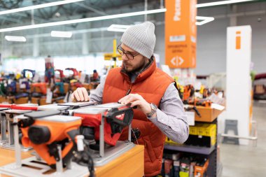 İnşaat aletleri hipermarketindeki bir müşteri elektrik planörlü bir rafın yanında..