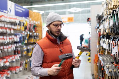 Bir adam inşaat hipermarketinde yeni bir çekiç seçer..