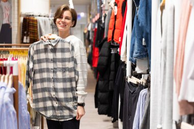 Genç bir kadın elbise mağazasında şık bir ekose gömlek deniyor..