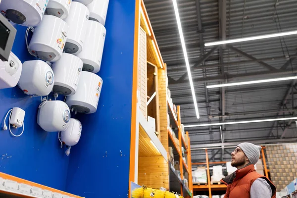 a customer in a plumbing hypermarket chooses a new hot water boiler for his home.