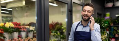 Çiçekçinin çalışanı telefonda konuşan bir gülümseme buketli bir buzdolabının yanında..