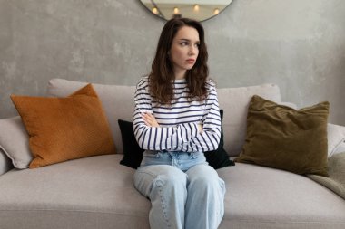 Kanepede oturan üzgün ve genç bir kadının portresi göğsünde çapraz kollarla..