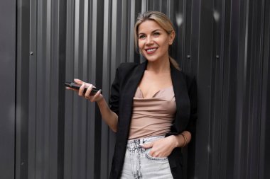 Çekici orta yaşlı bir iş kadını. Elinde gri bir duvarla büyüleyici bir gülümseme ile bir cep telefonu tutuyor..