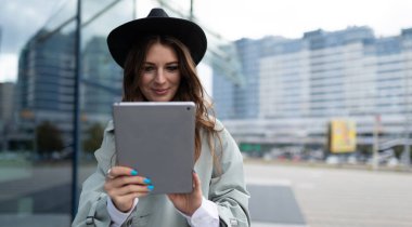 Şehirdeki bir ofis binasının yanındaki tablette çalışan genç bir kadın..