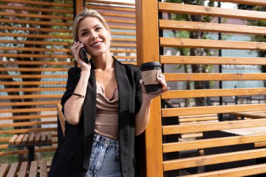 Orta yaşlı başarılı bir kadın bir kafede yemek molası sırasında telefonla konuşuyor ve kahve içiyor..