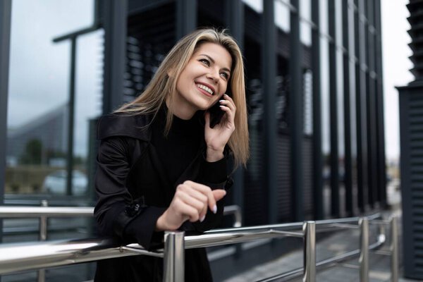 a middle-aged businesswoman woman has a business conversation on a mobile phone next to an office building.