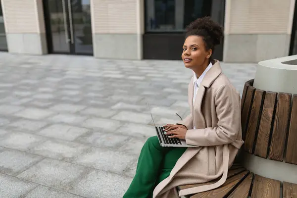 portrait of a successful young black woman with a laptop on a bench near the business center.
