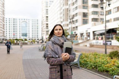 Şehrin arka planında dizüstü bilgisayarı ve defteri olan genç bir kız öğrenci..