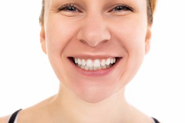 Dişleriyle gülümseyen ve beyaz arka plandaki kameraya cilveli bir şekilde bakan genç bir kadın..