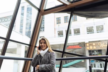 Şık bir kadın iş kadını, bir iş binasının arka planında cep telefonuyla konuşuyor..