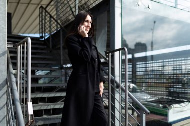 Genç, hırslı kadın kafası cep telefonuyla konuşuyor. Güçlü bir ofis binasının arka planına karşı..