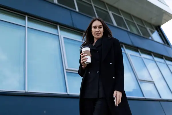 portrait of a strong successful business woman in a black business coat on the background of the glass facade of the building.