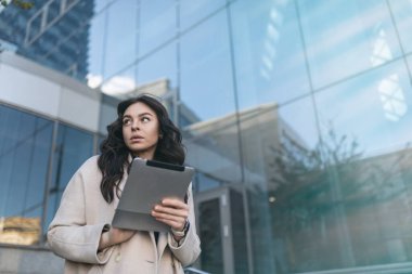 Elinde tabletle şık bir iş kadını bir ofis gökdeleninin zeminine yaslanmış..