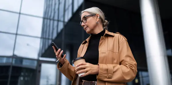 stylish elderly woman with a mobile phone and a glass of coffee on the background of a modern business center.