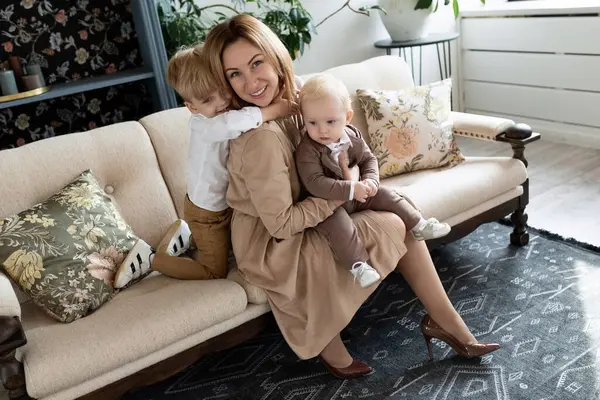 happy mom sitting on sofa in stylish clothes with two cute sons.