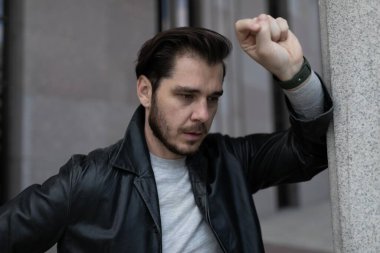 Yüzünde acı ve üzüntü dolu bir adam dirseğini binanın duvarına dayamış duruyor..