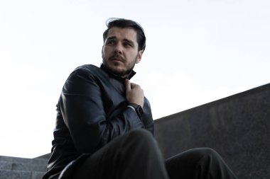 Depresyondaki üzgün adam gri duvarın yanındaki siyah basamaklarda oturuyor..