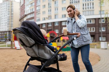 Bebek arabasıyla çocuk parkında gezen genç bir anne. Müzik dinler ve bir fincan kahve içerim.