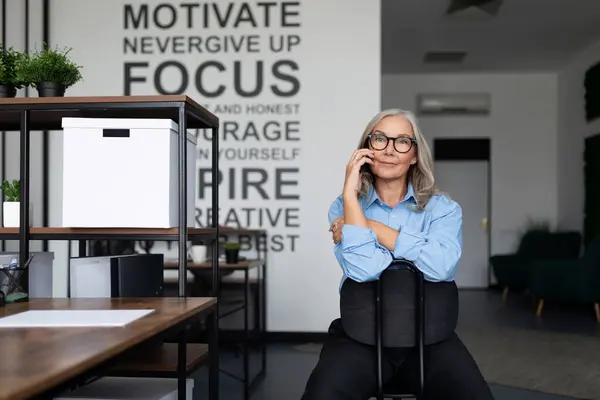 adult woman executive talking on a mobile phone while sitting on a chair backwards in the office.