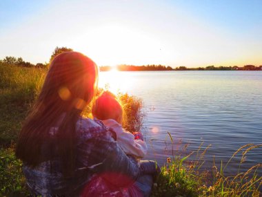 Anne ve kızı, sıcak ve güneşli bir akşamda göl kenarındaki yaz günbatımına hayran kalırlar..