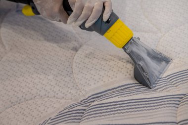 İşçi, elektrikli süpürgeyle yatak temizliyor. Çıkarma yöntemi..