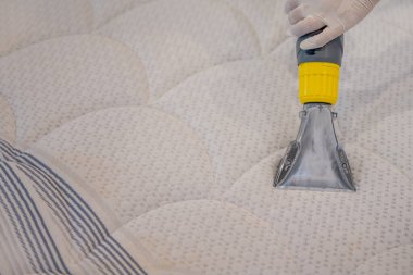 İşçi, elektrikli süpürgeyle yatak temizliyor. Çıkarma yöntemi..
