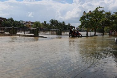 Hoi An, Vietnam, 25 Ekim 2021: 2021 yağmur sezonu boyunca Vietnam 'ın orta kesimindeki Hoi An kentinde su basmış bir sokakta motosikletli iki kişi