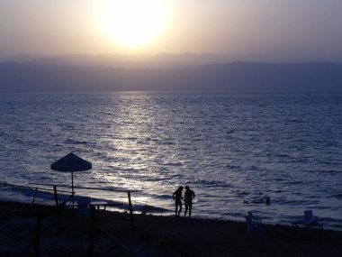 Ölü Deniz, Ürdün, 9 Ağustos 2010: Ürdün 'deki Ölü Deniz kıyısındaki sakin bir sahilde bir çift gün batımında yürür
