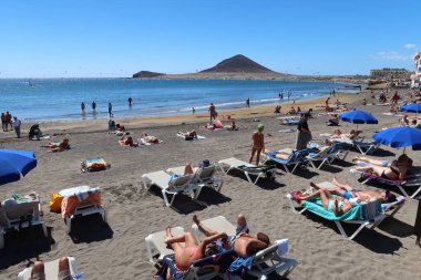 El Medano, Tenerife, İspanya, 8 Mart 2022: Turistler arka planda Kızıl Dağ ile El Medano 'nun volkanik kumsalında güneşleniyor. Tenerife, İspanya