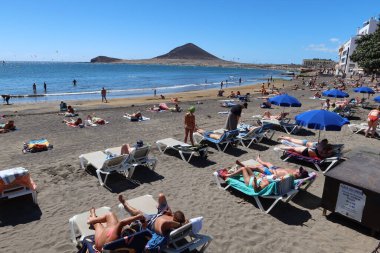 El Medano, Tenerife, İspanya, 8 Mart 2022: Birçok turist arka planda Kızıl Dağ ile birlikte El Medano 'nun volkanik kumsalında güneşleniyor. Tenerife, İspanya