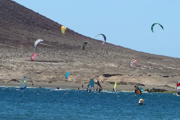 El Medano, Tenerife, Spain, March 8, 2022: Fans practicing kitesurfing on the Red Mountain volcanic sand beach of el Medano, Tenerife, Spain