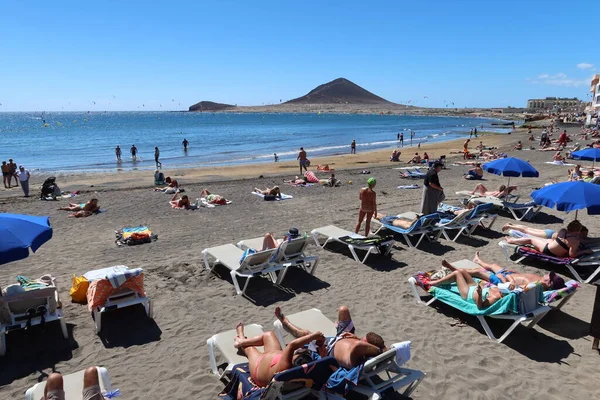 El Medano, Tenerife, İspanya, 8 Mart 2022: Turistler arka planda Kızıl Dağ ile El Medano 'nun volkanik kumsalında güneşleniyor. Tenerife, İspanya