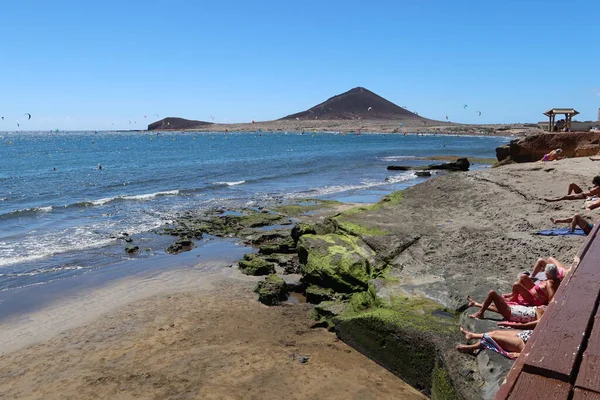 El Medano, Tenerife, İspanya, 8 Mart 2022: Birçok insan arka planda Kızıl Dağ ile birlikte El Medano 'nun volkanik kumsalında güneşleniyor. Tenerife, İspanya