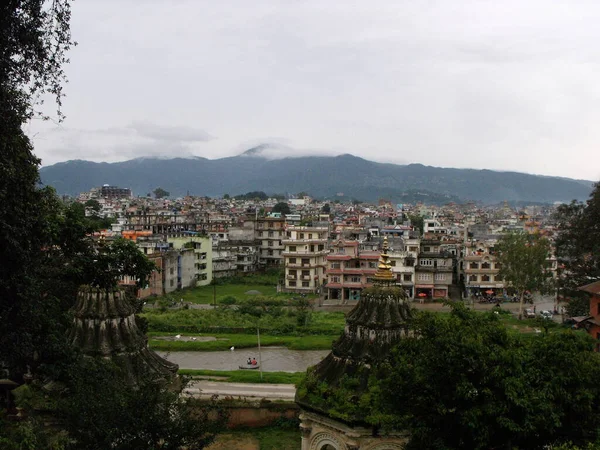 Kathmandu, Nepal, August 19, 2011: Buildings between two pagodas along the Bagmati River with the Himalayas in the background in Kathmandu, Nepal