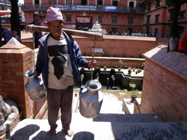 Durbar Square, Patan, Kathmandu, Nepal, August 20, 2011: An elderly man carries two pots in Durbar Square, Patan, Kathmandu, Nepal