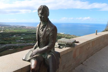 La Orotava, Tenerife, Spain, February 23, 2022: Sculpture of the German naturalist Alexander Von Humboldt and his famous treatise at the Humboldt viewpoint with the Atlantic Ocean in the background. La Orotava, Tenerife. Spain